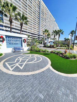 Entrada de hotel com um grande letreiro, palmeiras e um espaço pavimentado com um design circular.
