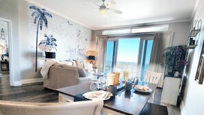A modern living room with a dining area, a ceiling fan, and a large window offering a view. - Exceptional unit! Extra large offering the best set up and views! (Panama City Beach)