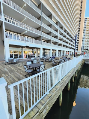 A multi-story hotel with outdoor dining areas on a wooden deck, overlooking a body of water. - Extremely Convenient 2nd FLOOR! No elevators needed! Perfect  beach getaway! (Panama City Beach)