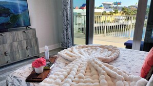 Un dormitorio con una cama grande, un televisor en la pared y vistas a un balcón con barandilla.