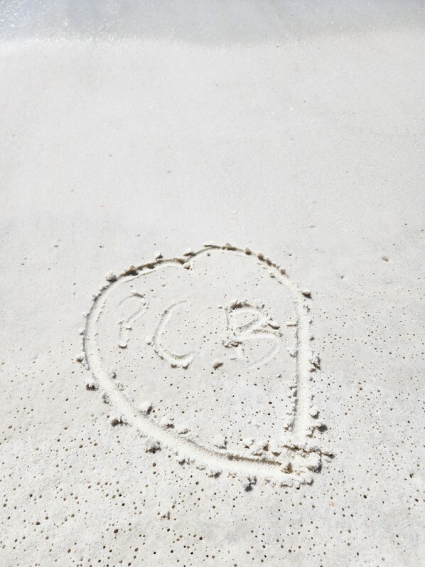 A sandy beach with footprints and a heart shape drawn in the sand.