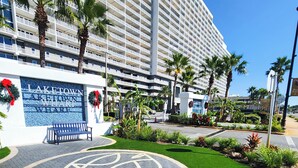 A hotel entrance with a large sign, palm trees, and a paved area with a circular design.