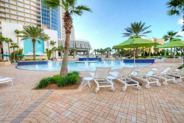 A pool area with lounge chairs and umbrellas, surrounded by palm trees and a building with a sign that reads 'SPLASH BAR'. - Best accessible unit on 3rd FLOOR! Gorgeous! Convenient! Heavenly! (Panama City Beach)