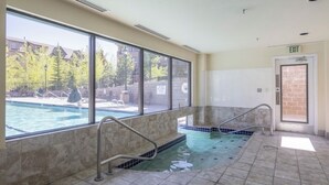 Un área de spa con una bañera de hidromasaje, una ventana con vistas a árboles y edificios, y una puerta de salida.