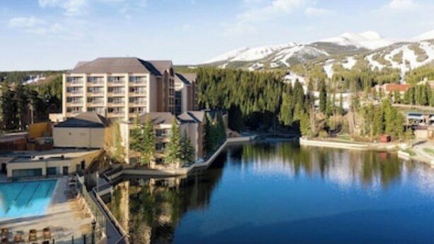 Un hotel con piscina, montañas al fondo y un lago.