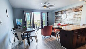 A modern kitchen with a stone backsplash, a dining area with a round table and chairs, and a balcony with curtains.