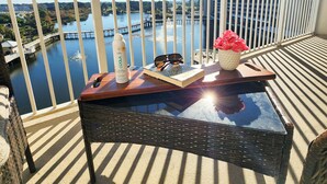 Een balkon met uitzicht op een meer, een boek, zonnebril en een colabottle op een tafel.