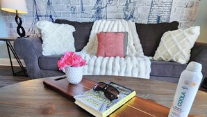 Ein gemütliches Wohnzimmer mit einem Holztisch, einem Buch, einer Kerze und einer Flasche Mineralwasser.