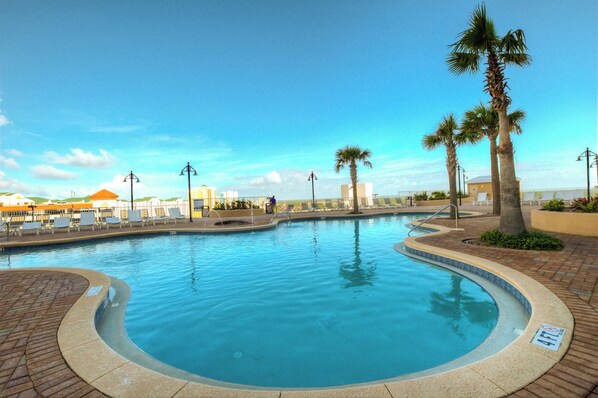 Enjoy a refreshing swim in our resort's inviting pool surrounded by palm trees and a paved walkway.