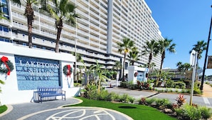 Entrada de hotel com um grande letreiro, palmeiras e um espaço pavimentado com um design circular.