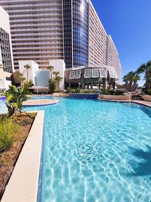 Un hotel con piscina, palmeras y un edificio moderno con balcones.