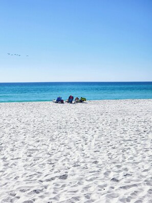 Una playa arenosa con tres sillas de playa y una sombrilla azul.
