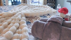 A room with a bed covered in a white fluffy blanket, a grey blanket, and a patterned bedspread. There is a water bottle and a vase with red flowers on a table. - Gorgeous Unit, Best amenities with a private boardwalk and multiple pools!! (Panama City Beach)
