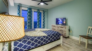 Un dormitorio con cama, ventilador de techo, televisor y una silla.