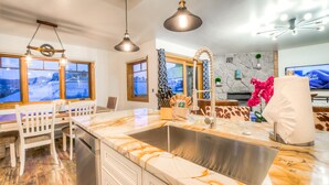 A modern kitchen with a marble countertop, stainless steel sink, and pendant lighting.