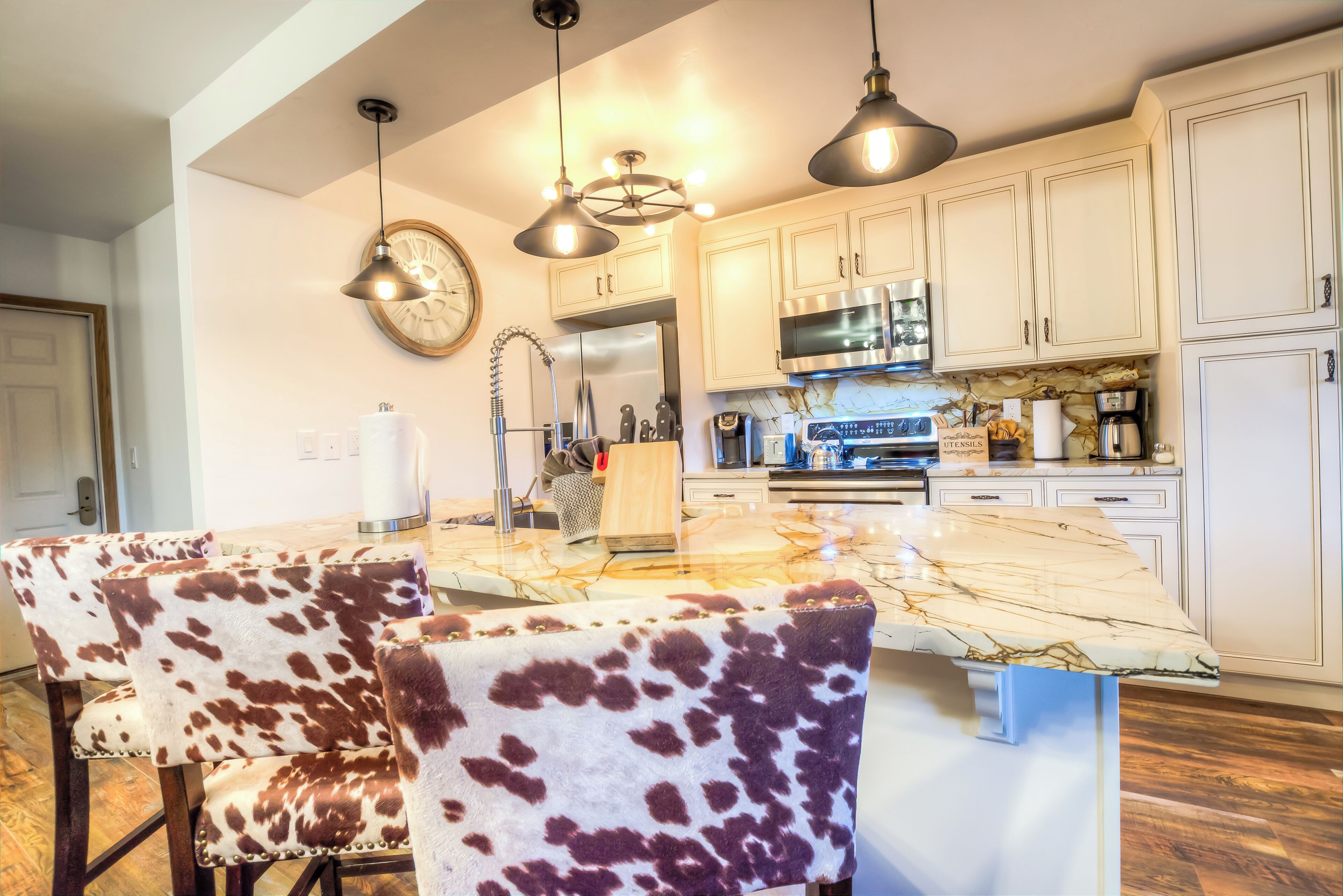 Une cuisine moderne avec des armoires blanches, un îlot en marbre et des luminaires suspendus.
