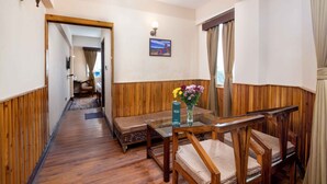 A hotel room with a wooden floor, a sofa, a glass table, and a vase with flowers. - Muscatel Roma (Darjeeling)