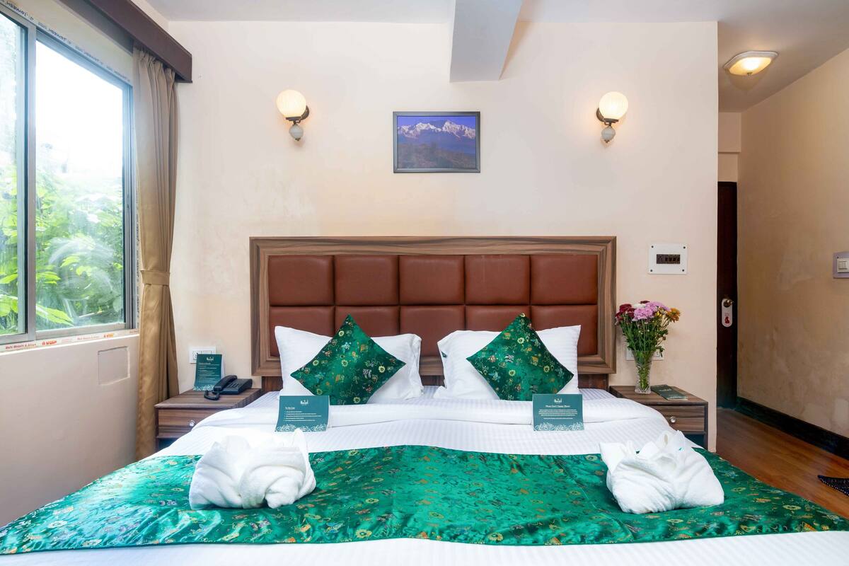 A hotel room with a large bed, two wall-mounted lights, a framed picture on the wall, a nightstand with a phone, and a vase with flowers.