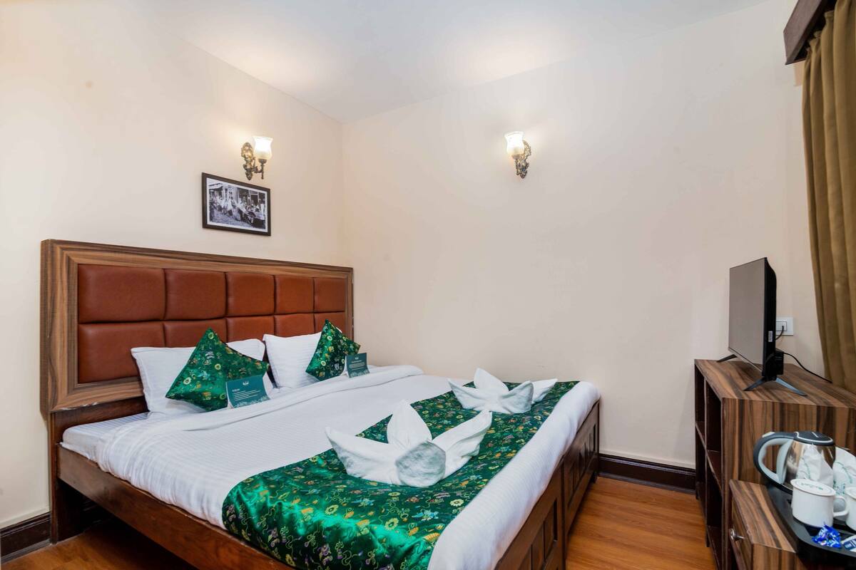 A hotel room with a bed, a television, and a tray with a kettle and cups.