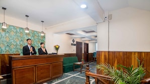 A reception area with a wooden reception desk, a green sofa, and a staircase with a wooden railing. - Muscatel Roma (Darjeeling)