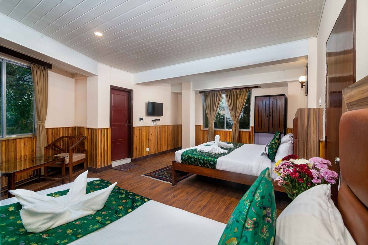 A hotel room with two beds, a TV, wooden walls, and a window with curtains.