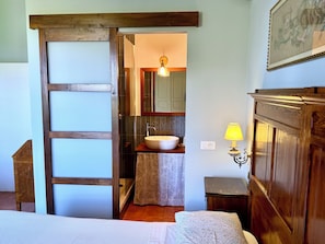 Una camera da letto con una porta in legno, un letto con copripiumino bianco, un comodino e una lampada da notte.