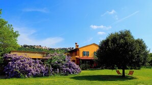 A house with a garden, a tree, and a view of a hill with buildings. - Belvedere Farmhouse: 2 Bedrooms, 2 Bathrooms, AC | Bolgheri & Sea at 10 minutes (Castagneto Carducci)