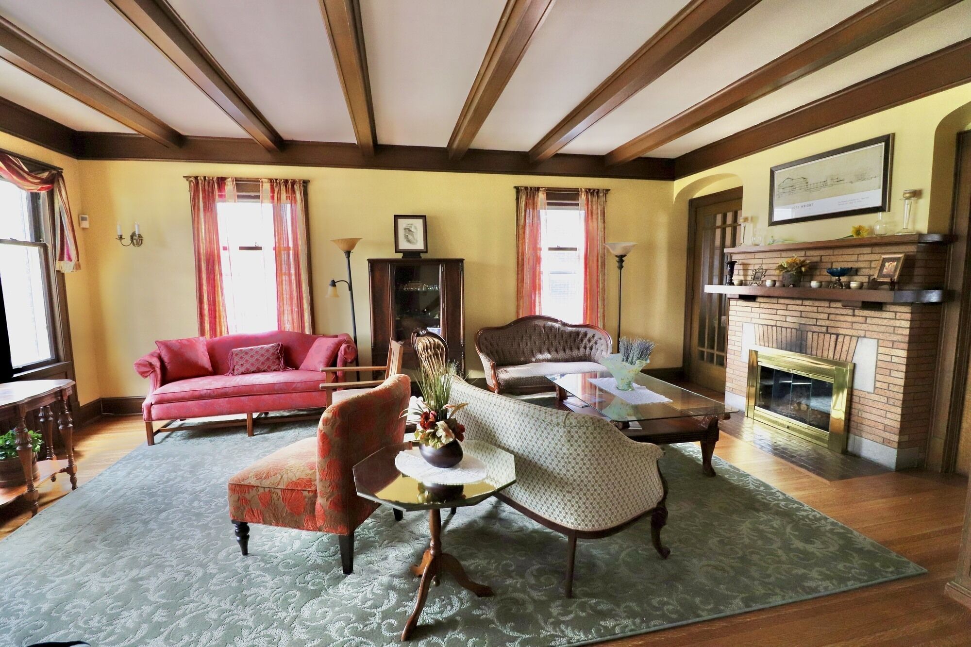 A traditional living room with a fireplace, a red sofa, a patterned armchair, and a coffee table.