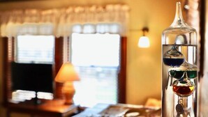 A room with a large window, a lamp on a side table, and a decorative glass bottle with colored liquids. - The Marshall Room w/ queen bed (Niagara Falls)