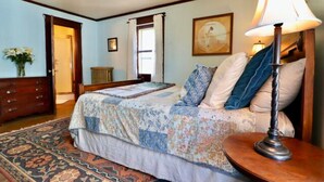 Un dormitorio con una cama, una mesita de noche, una lámpara, un aparador y una puerta.