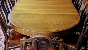 Una gran mesa de comedor de madera rodeada de sillas tapizadas en una habitación con paneles de madera y una alfombra estampada.