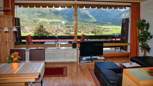 Sala de estar com uma grande janela que oferece vista para as montanhas, televisão e opções de assento.