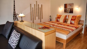 Quarto moderno com cama, sofá, abajur e parede com ripas de madeira verticais.