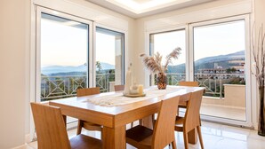 Un coin repas avec une table et des chaises en bois, de grandes fenêtres offrant une vue sur les montagnes et un vase décoré de plumes d’herbe de la pampa.