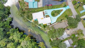An aerial view of a residential area with a large house featuring a blue roof, a driveway, and a small pond. - Manatee Cove Apartment Star5Vacations (Weeki Wachee)