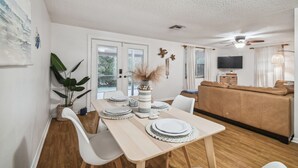 A dining area with a wooden table set for four, surrounded by white chairs. A large potted plant is on the left, and a vase with dried flowers is on the table. - Manatee Cove Apartment Star5Vacations (Weeki Wachee)