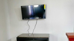 A room with a flat-screen TV mounted on the wall, a black cabinet with drawers, and a tiled floor. - Budget Inn, Hwy 41 (Barnesville)