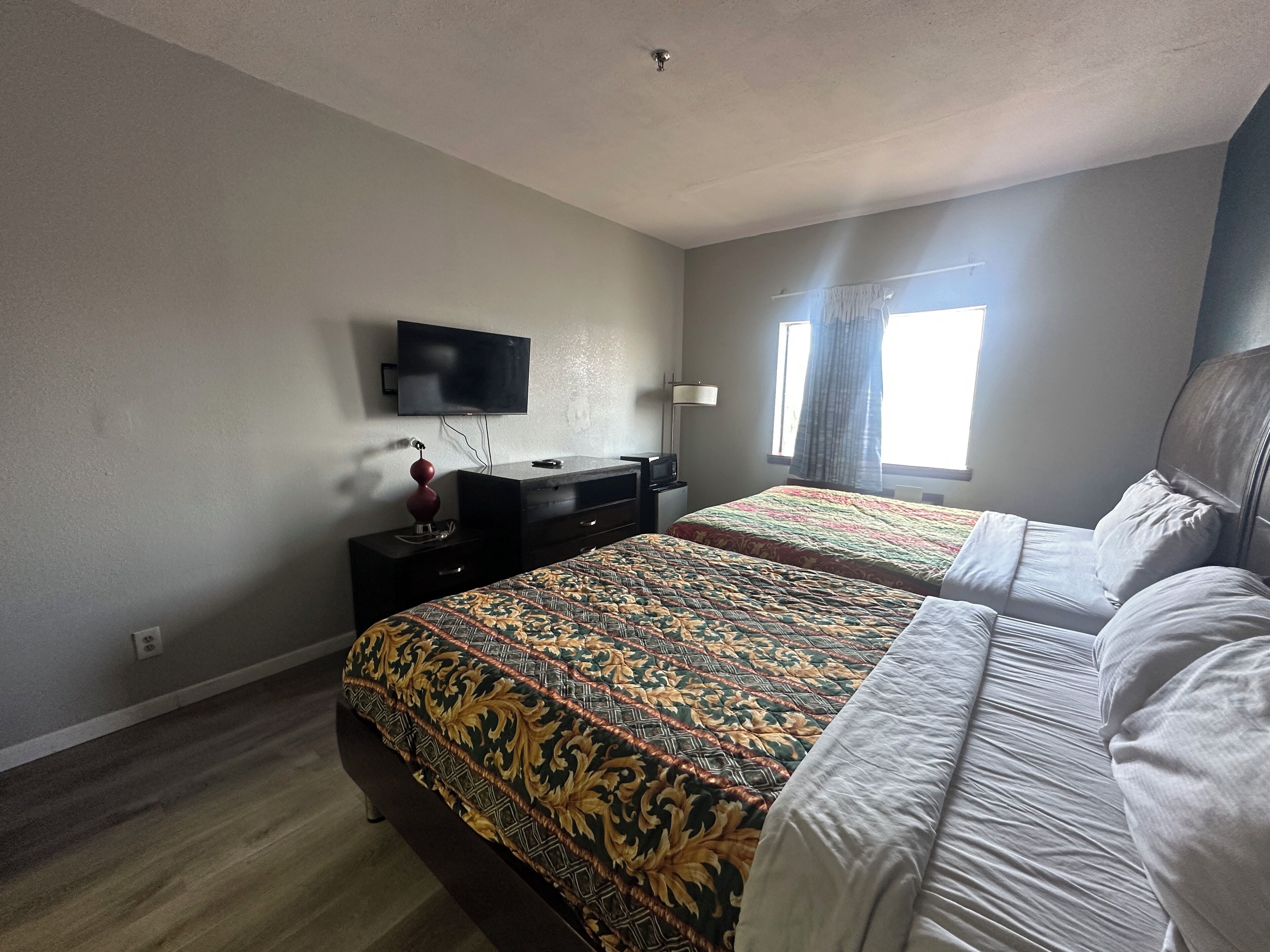 Habitación de hotel con dos camas, televisión, escritorio y ventana con cortinas.