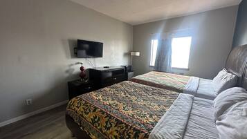 Habitación de hotel con dos camas, televisión, escritorio y ventana con cortinas.