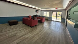 A spacious lobby with a red sofa set, a small brown ottoman, and a flat-screen TV mounted on the wall. - Budget Inn, Hwy 41 (Barnesville)