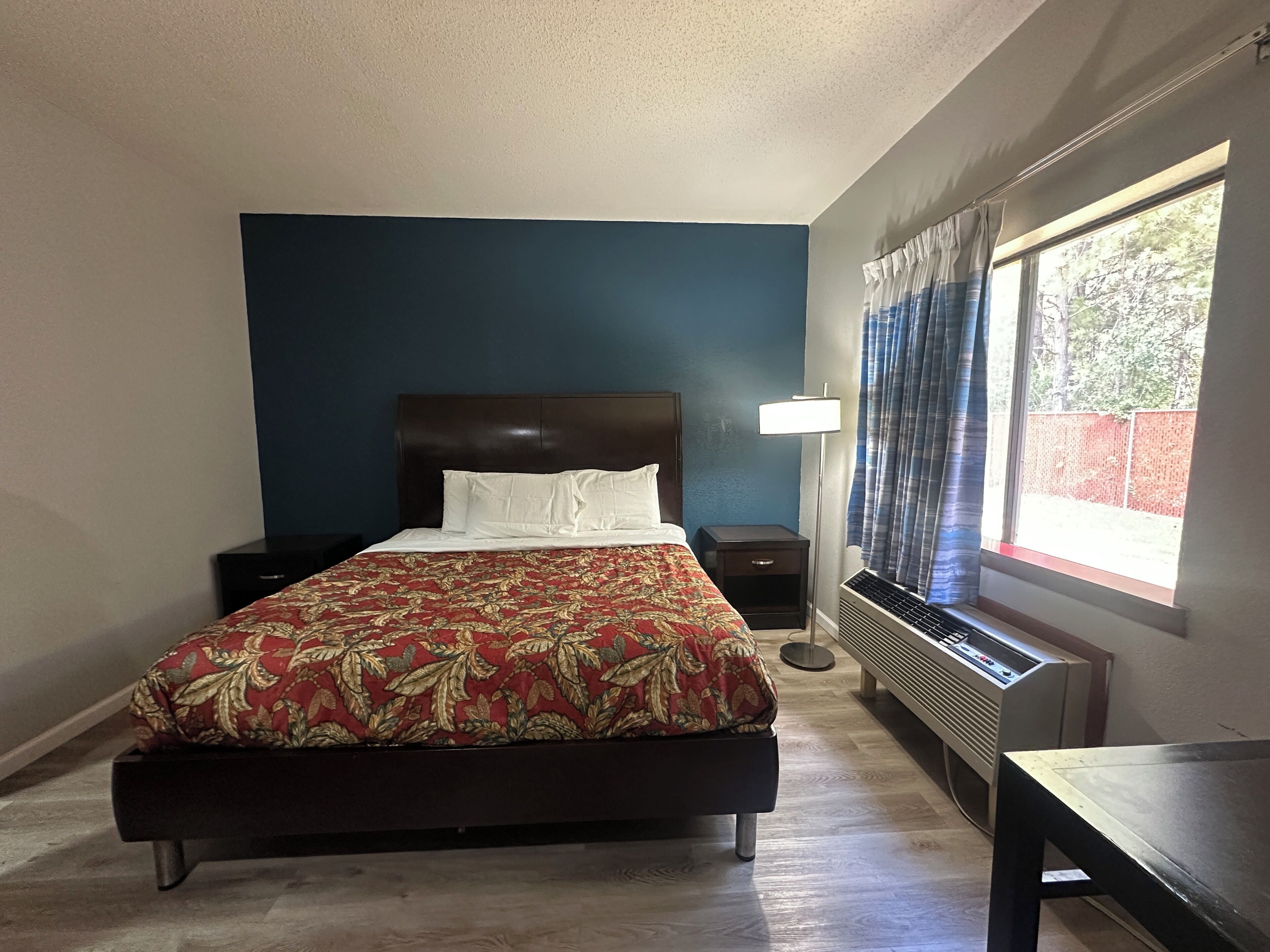 Un dormitorio con una cama grande, una mesita de noche, una lámpara, un calefactor y una ventana con cortinas.