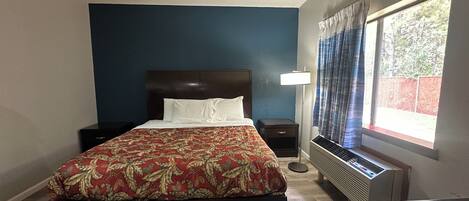 Un dormitorio con una cama grande, una mesita de noche, una lámpara, un calefactor y una ventana con cortinas.