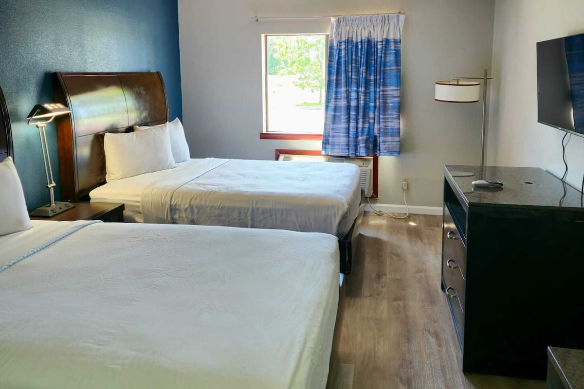 Une chambre d’hôtel avec deux lits, un bureau, une télévision et une fenêtre avec des rideaux.