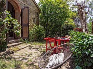 A rustic outdoor seating area with a wicker chair, a red table, and a brick wall with a wooden door. - Cozy little retreat in wonderful location, with pool (località Fornello, Pontassieve)