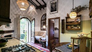 A cozy kitchen with a gas stove, wooden chairs, and a dining table. There are hanging lights and a bookshelf with books and decorative items. - Cozy little retreat in wonderful location, with pool (località Fornello, Pontassieve)