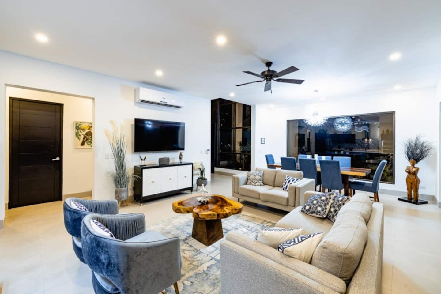 Una sala de estar moderna con un sofá, sillas, una mesa de centro, un televisor y un comedor con sillas y una mesa.