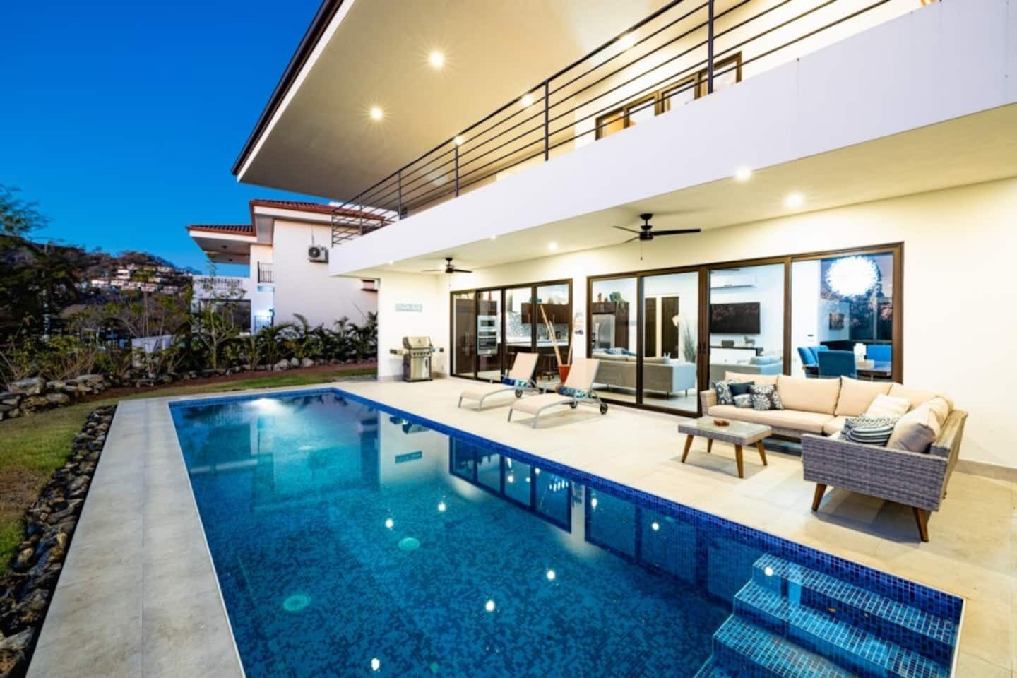 Una casa moderna con piscina, zona de estar exterior y balcón.