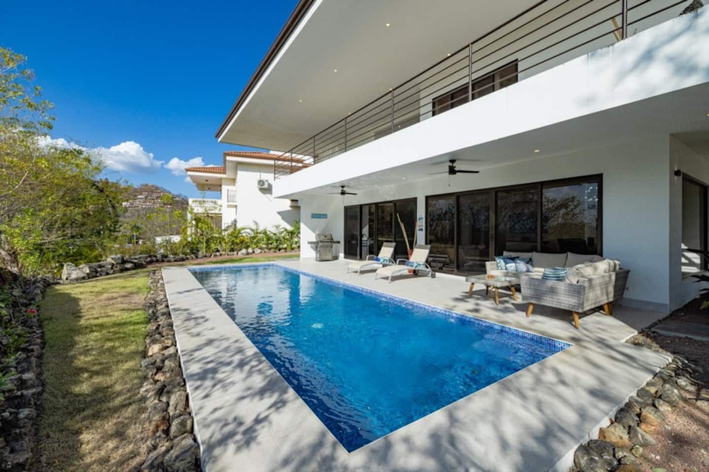 A modern house with a swimming pool, outdoor seating, and a stone wall.