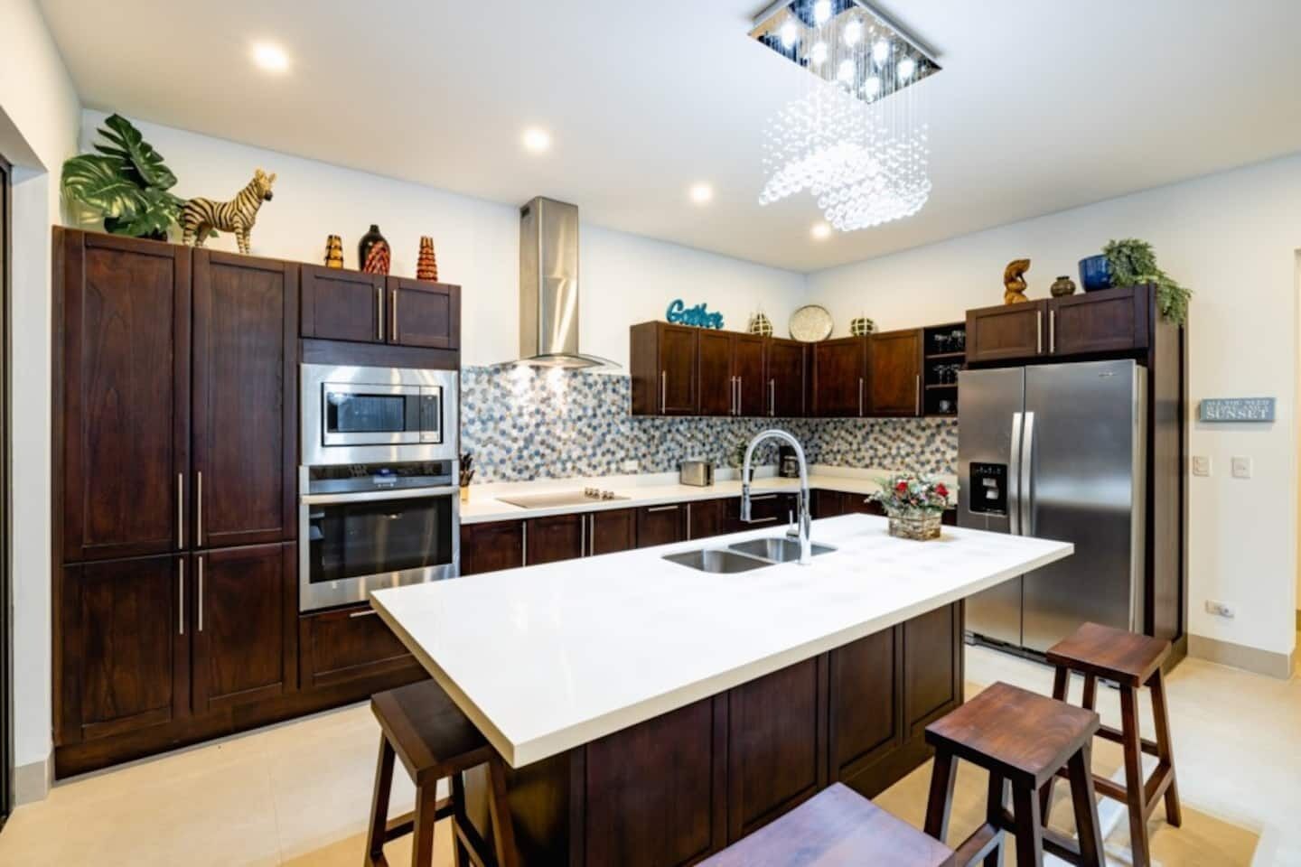 Una cocina moderna con armarios de madera oscura, electrodomésticos de acero inoxidable, una isla central con taburetes y objetos decorativos sobre las encimeras.