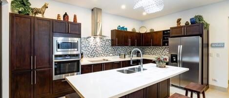 Una cocina moderna con armarios de madera oscura, electrodomésticos de acero inoxidable, una isla central con taburetes y objetos decorativos sobre las encimeras.